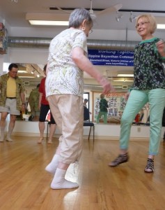 Photo: four seniors dancing, in twos facing each other, lifting up one foot