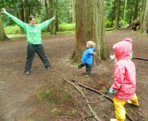 Photo: one adult and three children with arms wide, wearing rain gear in forest