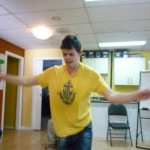 Photo: a man dancing facing the camera with both arms out to the sides, elbows slightly bent, and looking downward