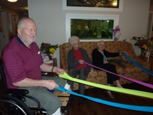 Photo: three older adults holding arms of a dance prop, plus a cat sitting on the couch.